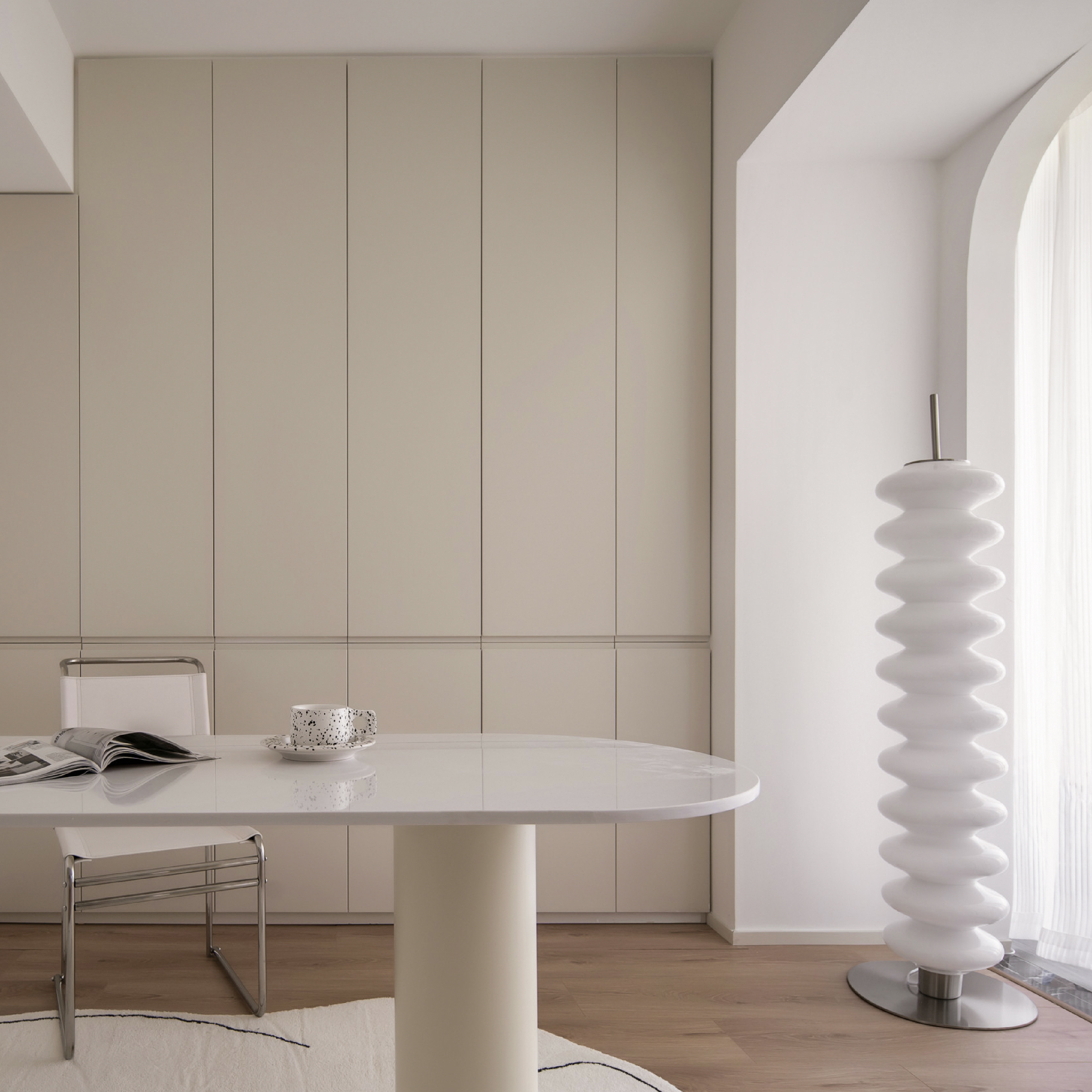 韓式奶油風空間範例：採用高明度的米色調大面積櫃牆作為視覺背景，搭配造型圓潤的白色長桌與極具設計感的螺旋狀地燈，透過簡潔的幾何線條與大量空間留白，展現出溫潤且充滿現代感的韓系生活美學。