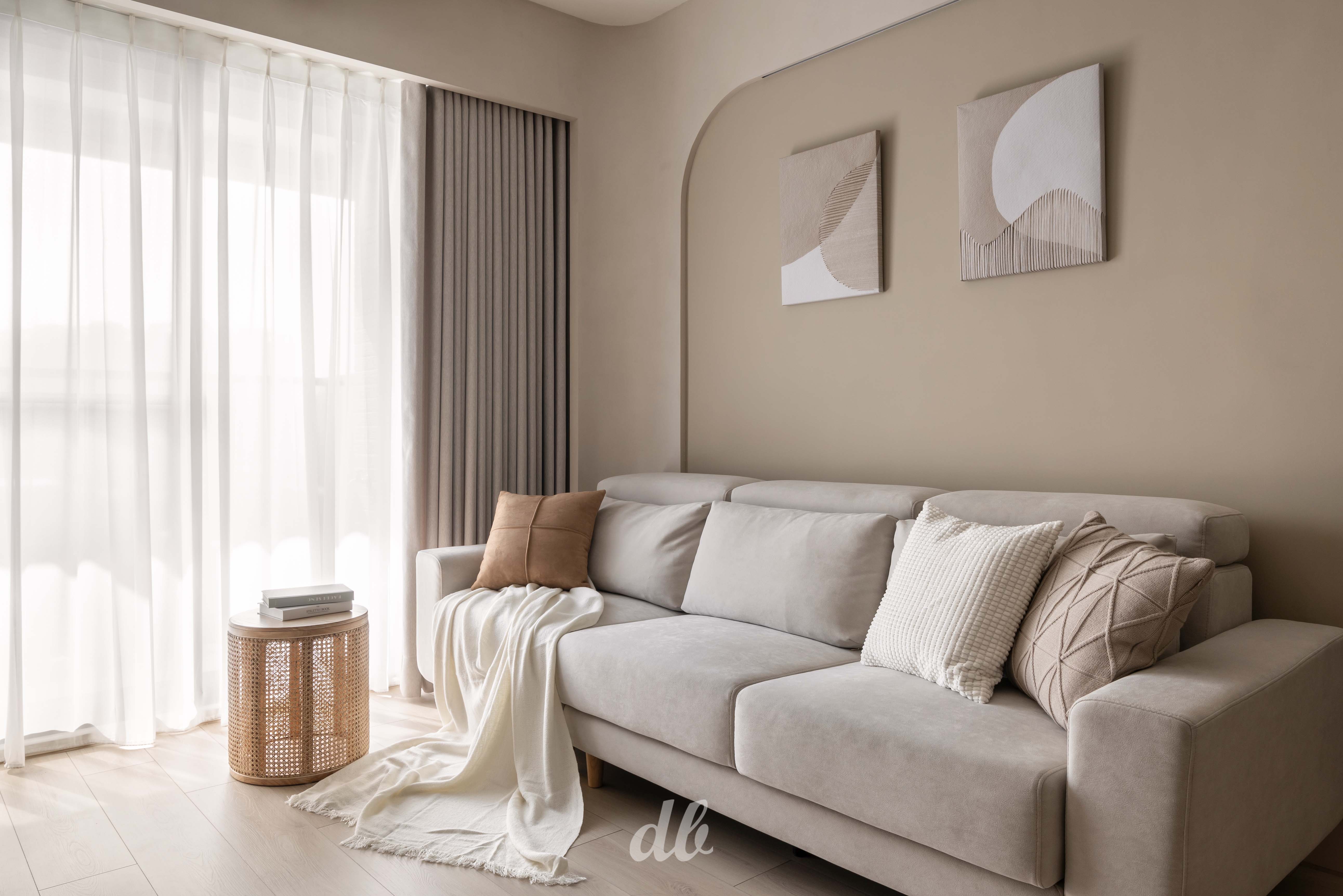 韓式奶油風客廳日造設計案例：暖米色調牆面嵌入圓弧造型壁燈，搭配柔軟布藝沙發與異材質針織毯，在紗簾柔光與低飽和色彩的映襯下，營造出具備豐富層次感且溫潤的日常居家氛圍。