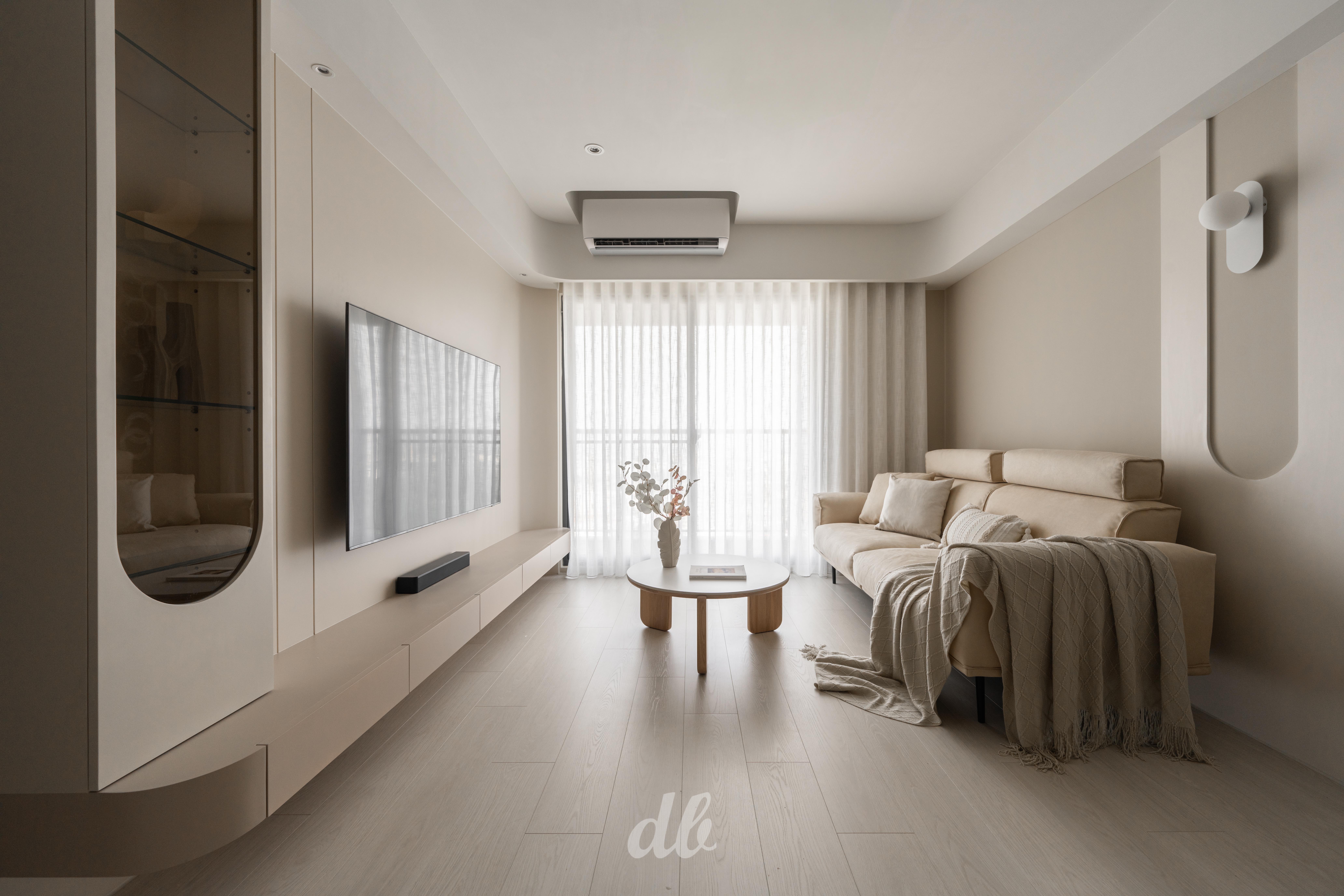 韓式奶油風客廳（日造設計案例）：以米杏色暖調為基底，配置圓弧收邊的懸空電視櫃與造型壁燈，透過弧形語彙引領流暢動線，並結合織物與木質軟裝打造溫潤且具層次感的韓系日常氛圍。