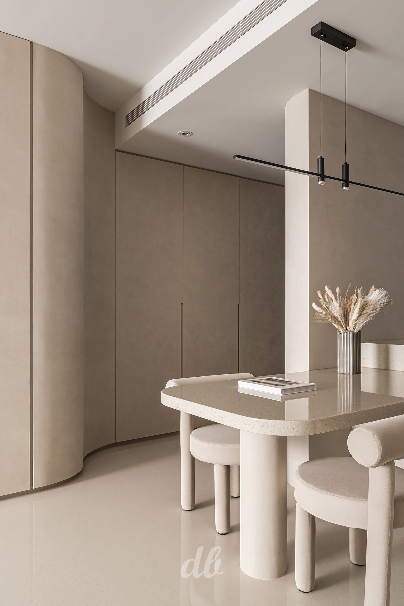 韓式奶油風空間日造設計案例：運用低飽和度的啞光麥色牆面與圓弧建築線條，搭配水磨石質感的圓角餐桌與造型圓柱餐椅，在極簡黑色線性吊燈的襯托下，完美詮釋空間的留白美學與溫潤生活氛圍。